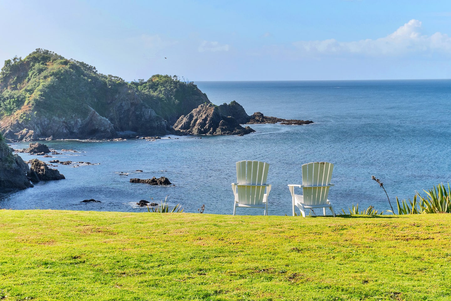 Two white chairs on the lawn looking out over the bay